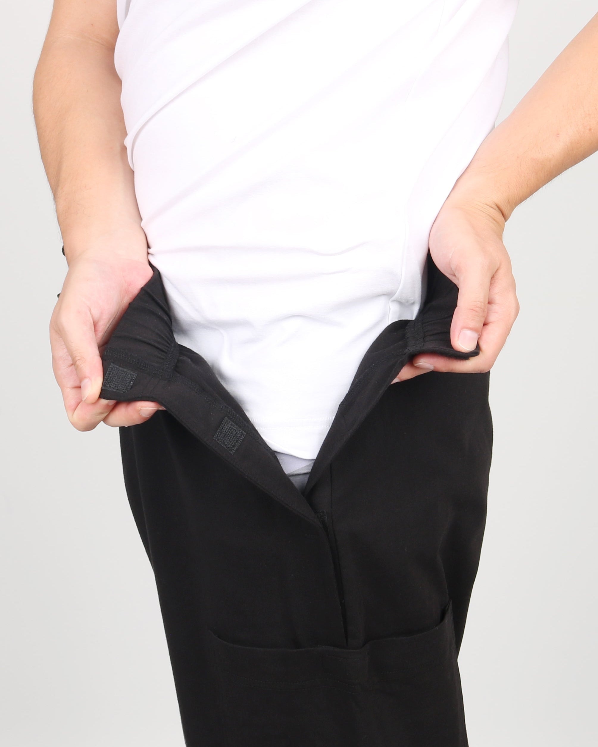 ComfortCure Adaptive Pflegehose für Prostatapatienten (mit Beintaschen), Schwarz, Vorderansicht, Hände öffnen den Klettverschluss am Bund