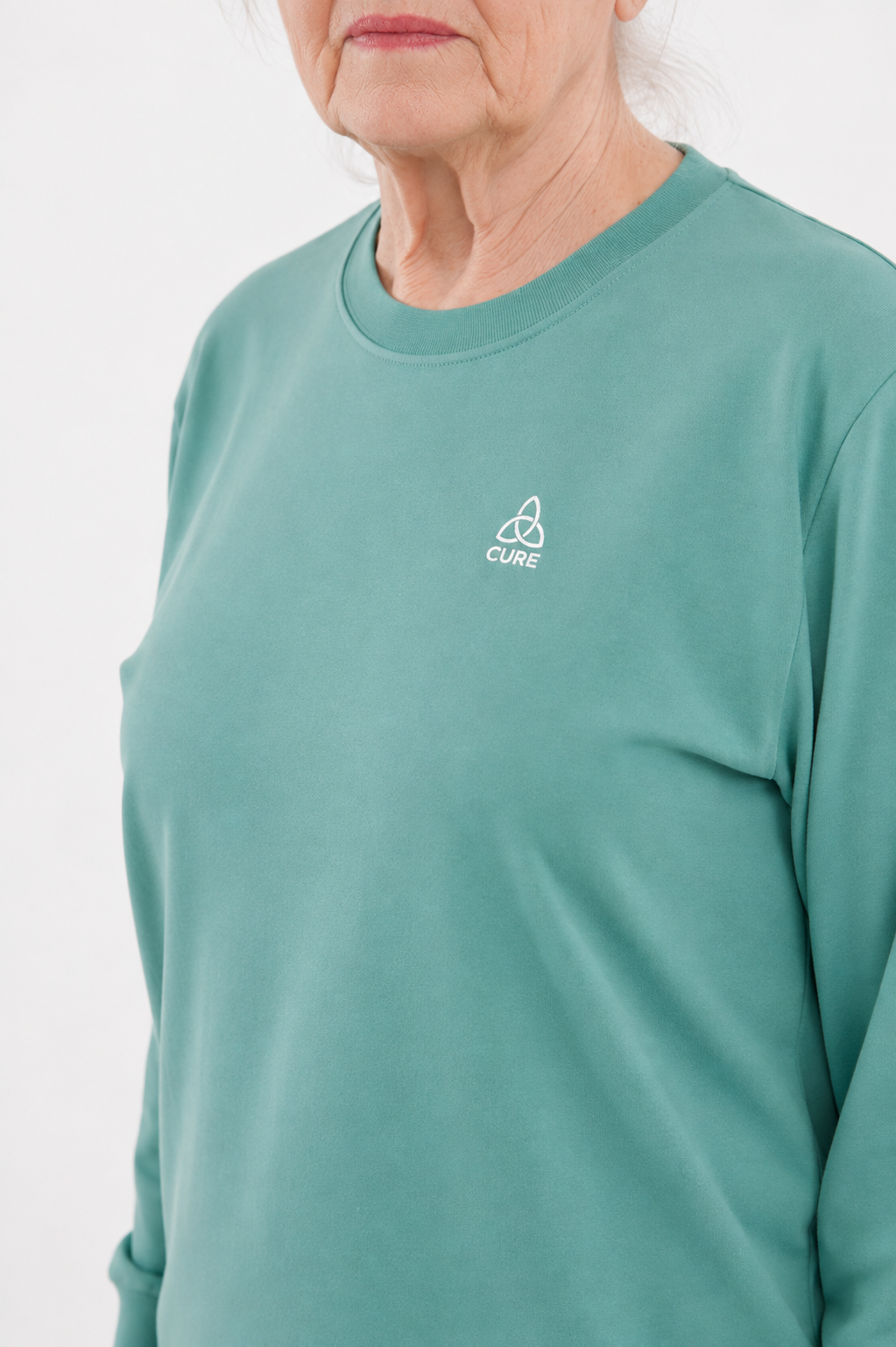 ComfortCure Adaptiver Pflegeoverall für die Alzheimer- und Demenzpflege, Grün, Detailansicht des Rundhalsausschnitts mit Logo auf der Brust