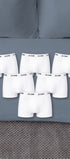 Sechs weiße ComfortCure Boxershorts auf einem Bett mit blaugrauer Bettwäsche