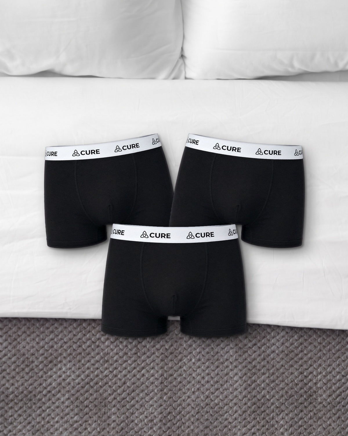 ComfortCure Alltags-Set, drei auslaufsichere Herren-Boxershorts in Schwarz, auf einem Bett liegend