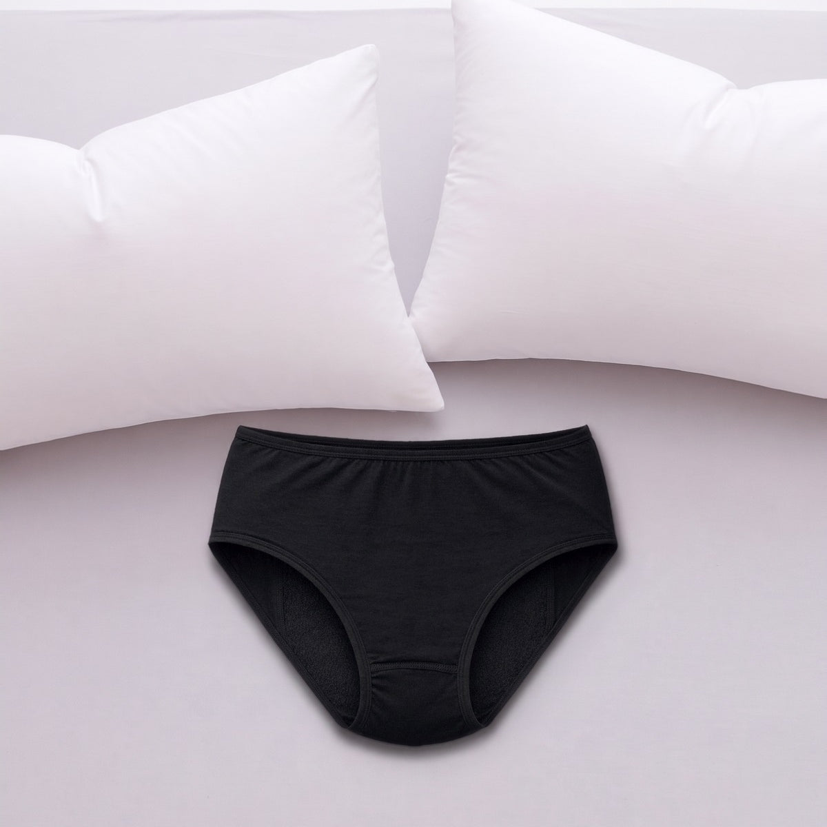 ComfortCure Adaptiver auslaufsicherer Damenslip, Schwarz, auf einem hellen Bett liegend