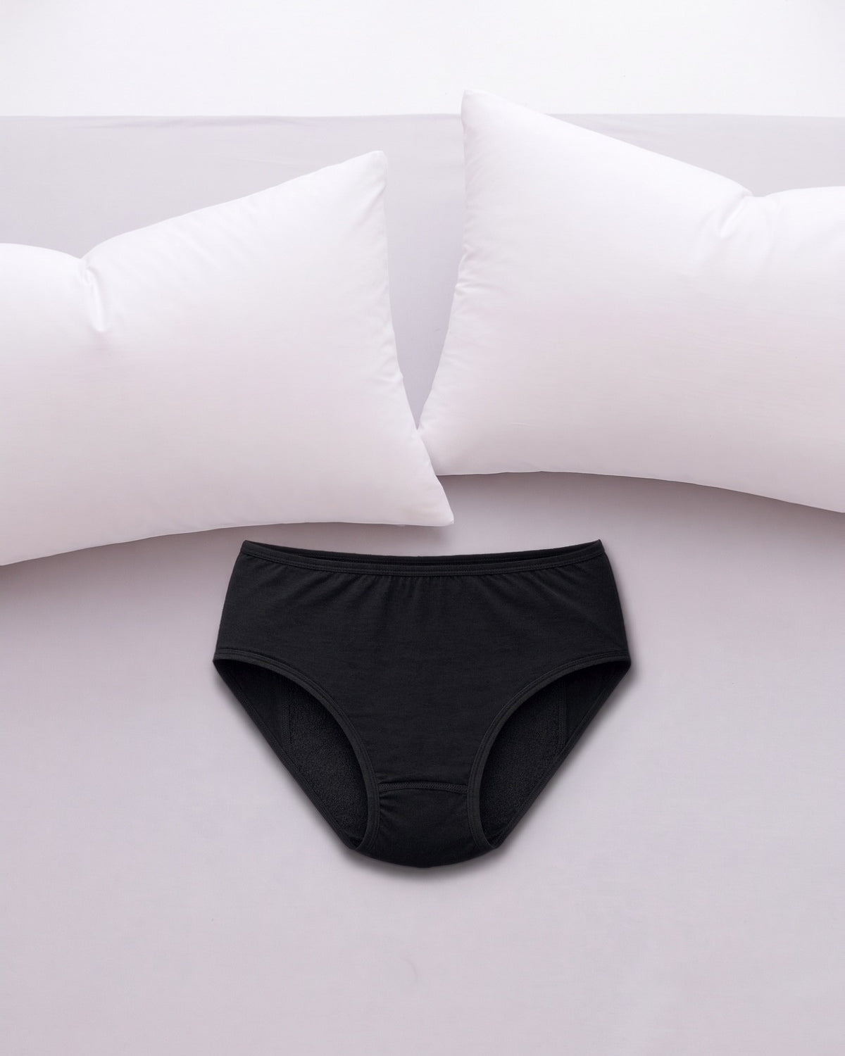 ComfortCure Adaptiver auslaufsicherer Damenslip, Schwarz, auf einem hellen Bett liegend