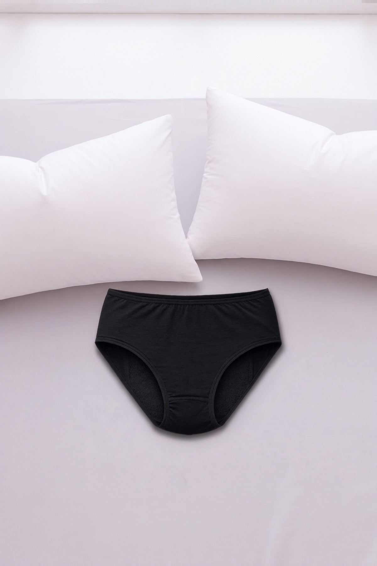 ComfortCure Adaptiver auslaufsicherer Damenslip, Schwarz, auf einem hellen Bett liegend
