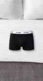 ComfortCure Herren-Boxershorts mit saugfähiger Innenschicht in Schwarz, liegen auf einem Bett mit weißen Kissen