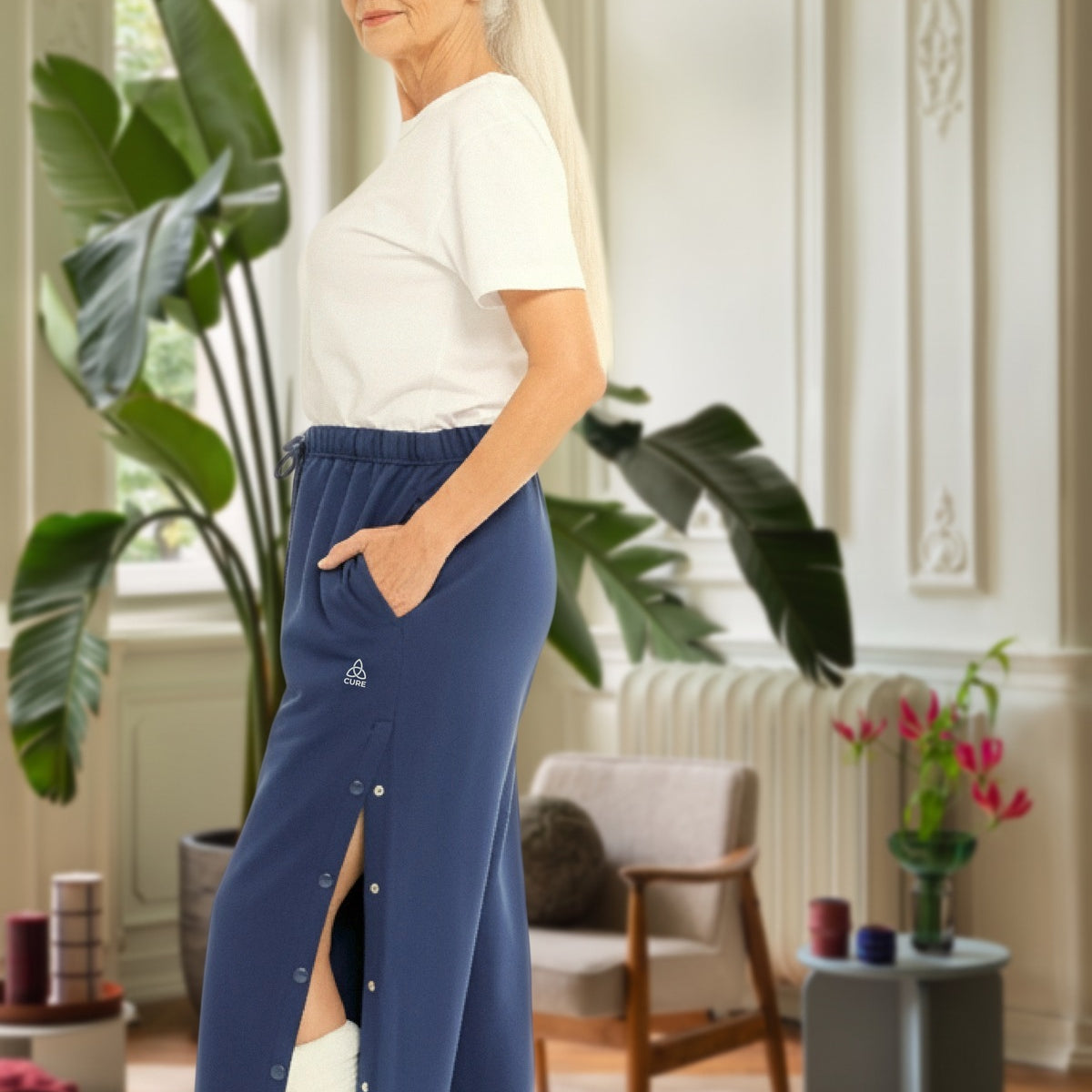 ComfortCure Adaptive Orthopädie-Pflegehose mit Druckknöpfen, Navy, Seitenansicht im Altbau-Wohnzimmer, seitlich geöffnet über einem bandagierten Bein