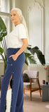 ComfortCure Adaptive Orthopädie-Pflegehose mit Druckknöpfen, Navy, Seitenansicht im Altbau-Wohnzimmer, seitlich geöffnet über einem bandagierten Bein