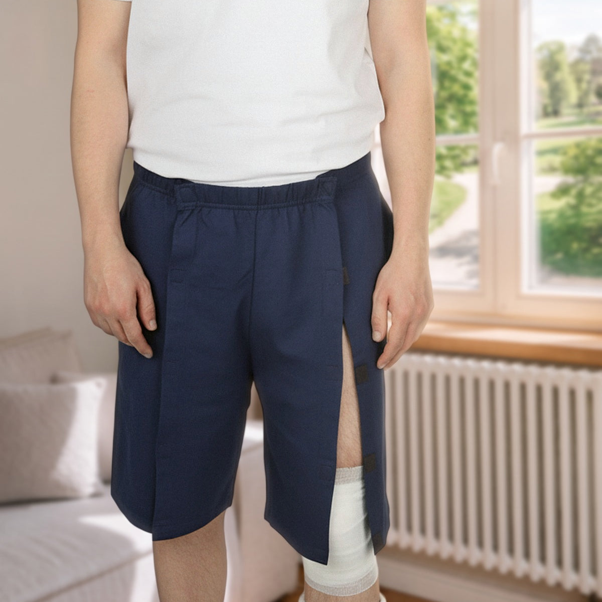 ComfortCure Adaptive Pflegeshorts für bettlägerige Patienten mit Klettverschluss, Navy, Vorderansicht im Wohnzimmer, seitlich geöffnet über einem Gipsbein