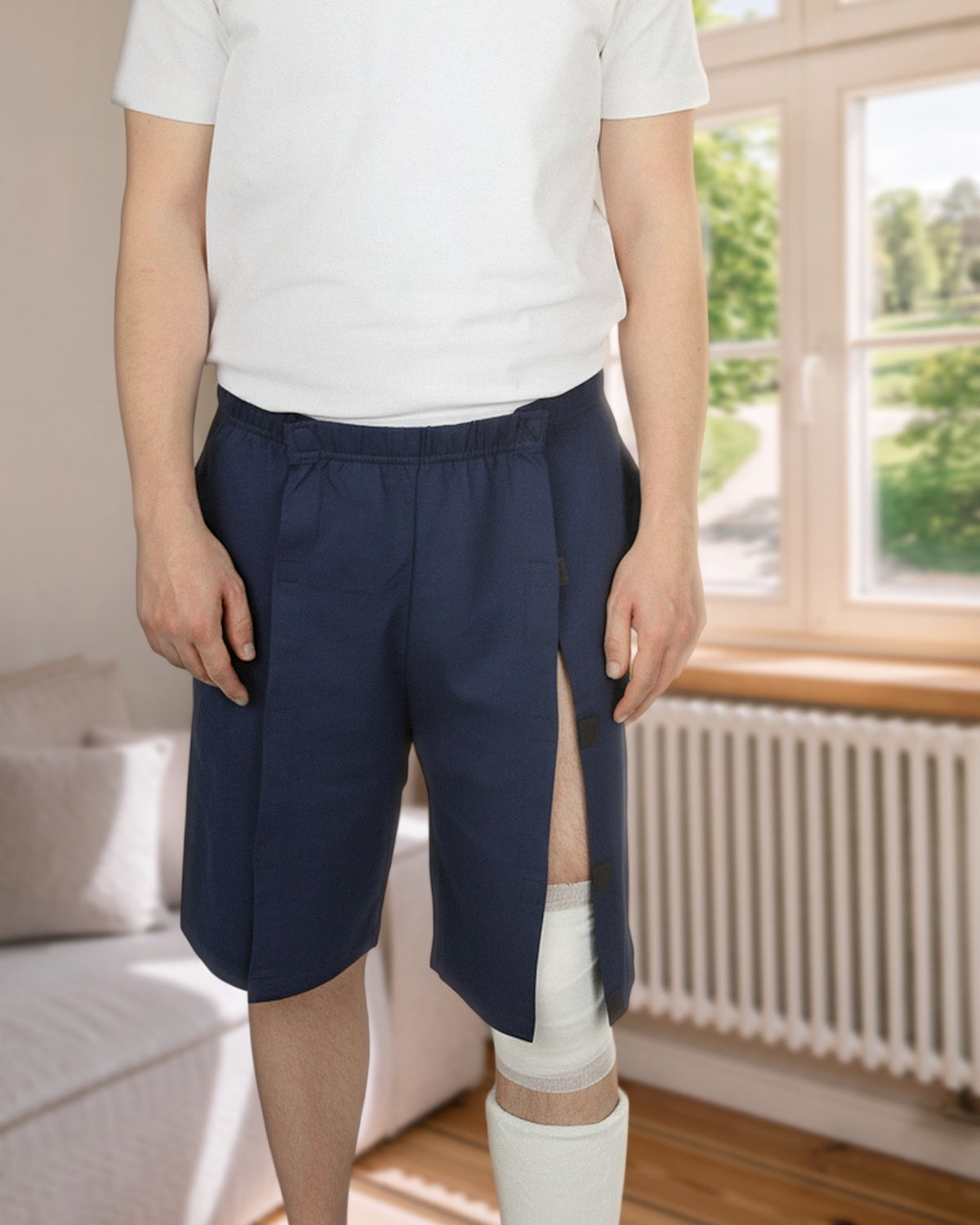 ComfortCure Adaptive Pflegeshorts für bettlägerige Patienten mit Klettverschluss, Navy, Vorderansicht im Wohnzimmer, seitlich geöffnet über einem Gipsbein
