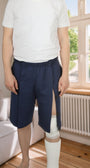 ComfortCure Adaptive Pflegeshorts für bettlägerige Patienten mit Klettverschluss, Navy, Vorderansicht im Wohnzimmer, seitlich geöffnet über einem Gipsbein