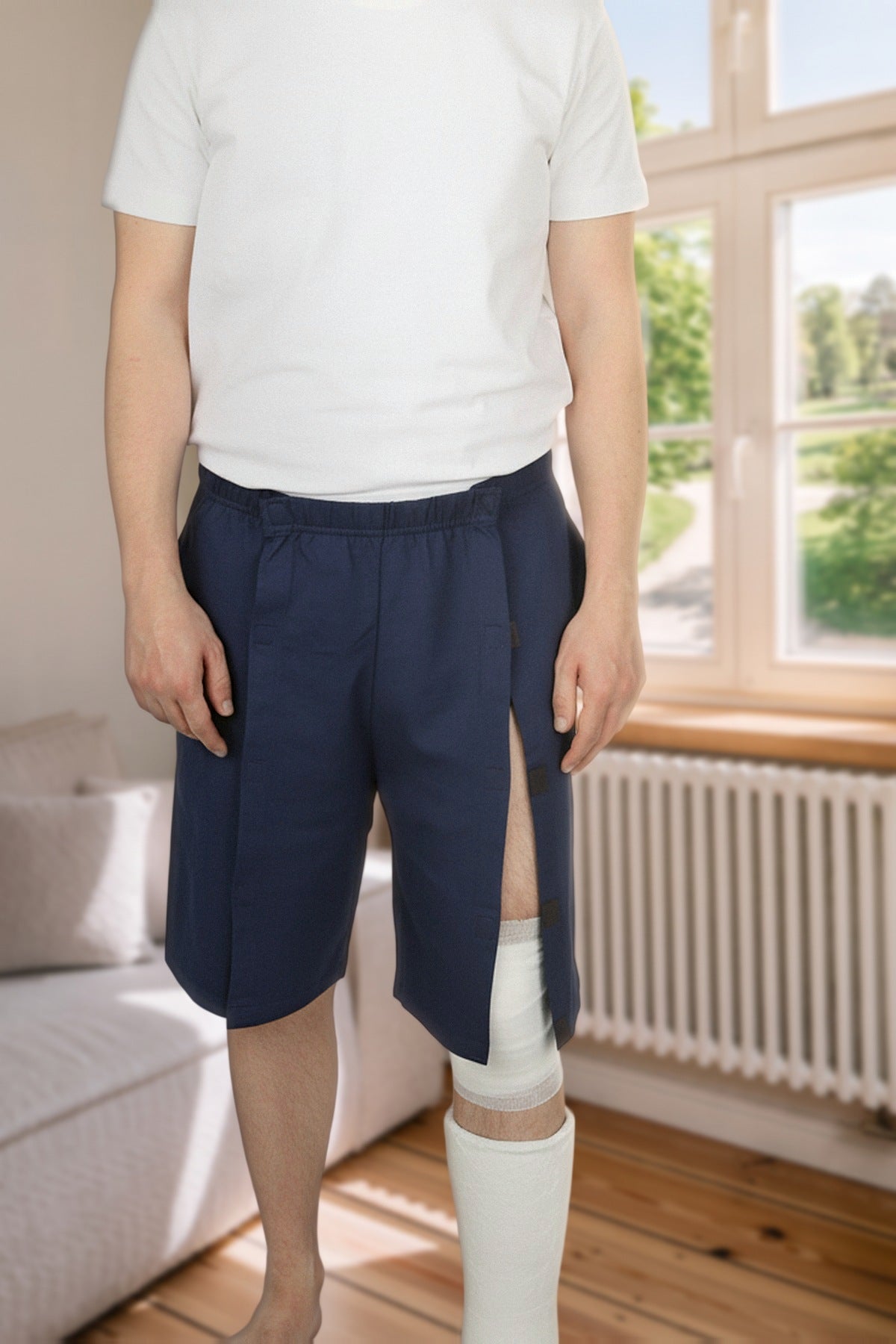 ComfortCure Adaptive Pflegeshorts für bettlägerige Patienten mit Klettverschluss, Navy, Vorderansicht im Wohnzimmer, seitlich geöffnet über einem Gipsbein
