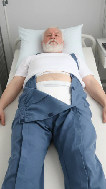 Älterer Mann liegt im Bett, blaue Pflegehose mit nach unten geklapptem Vorderteil und sichtbarer Inkontinenzvorlage