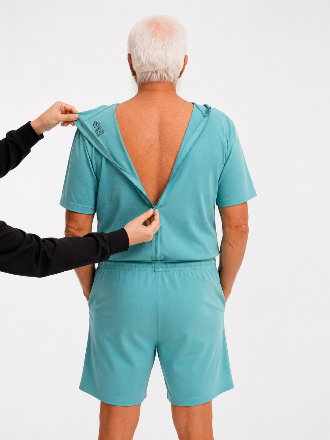 ComfortCure Adaptiver Kurzarm-Pflegeoverall für die Alzheimer- und Demenzpflege, Grün, Rückansicht, Pflegeperson öffnet den Rückenreißverschluss