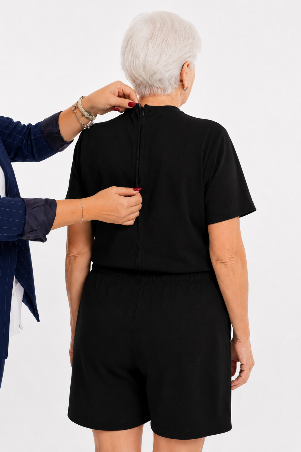ComfortCure Adaptiver Kurzarm-Pflegeoverall für die Alzheimer- und Demenzpflege, Schwarz, Rückansicht, Pflegeperson hält den geöffneten Rückenreißverschluss