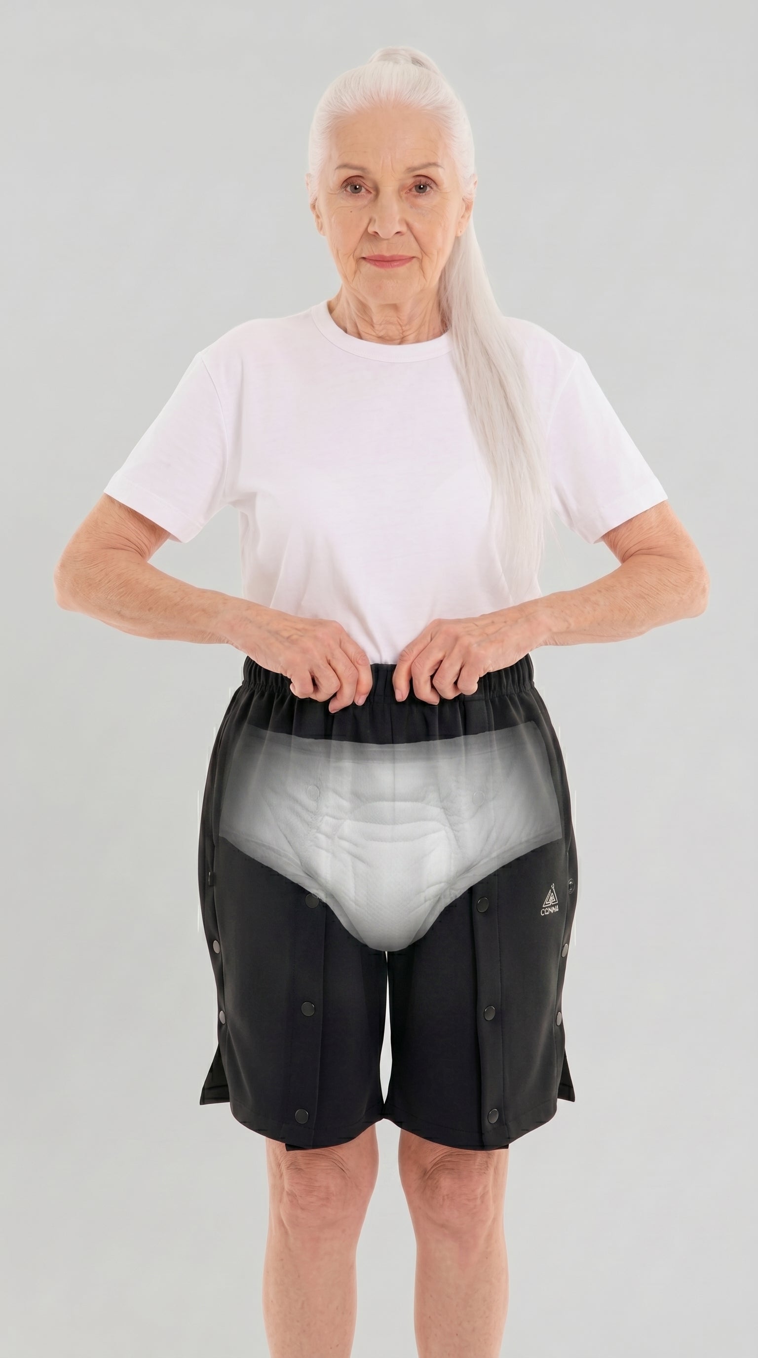 ComfortCure Adaptive Pflegeshorts für bettlägerige Patienten - mit Druckknöpfen, Grau meliert, Vorderansicht mit transparenter Einblendung der Inkontinenzvorlage, Hände am Bund
