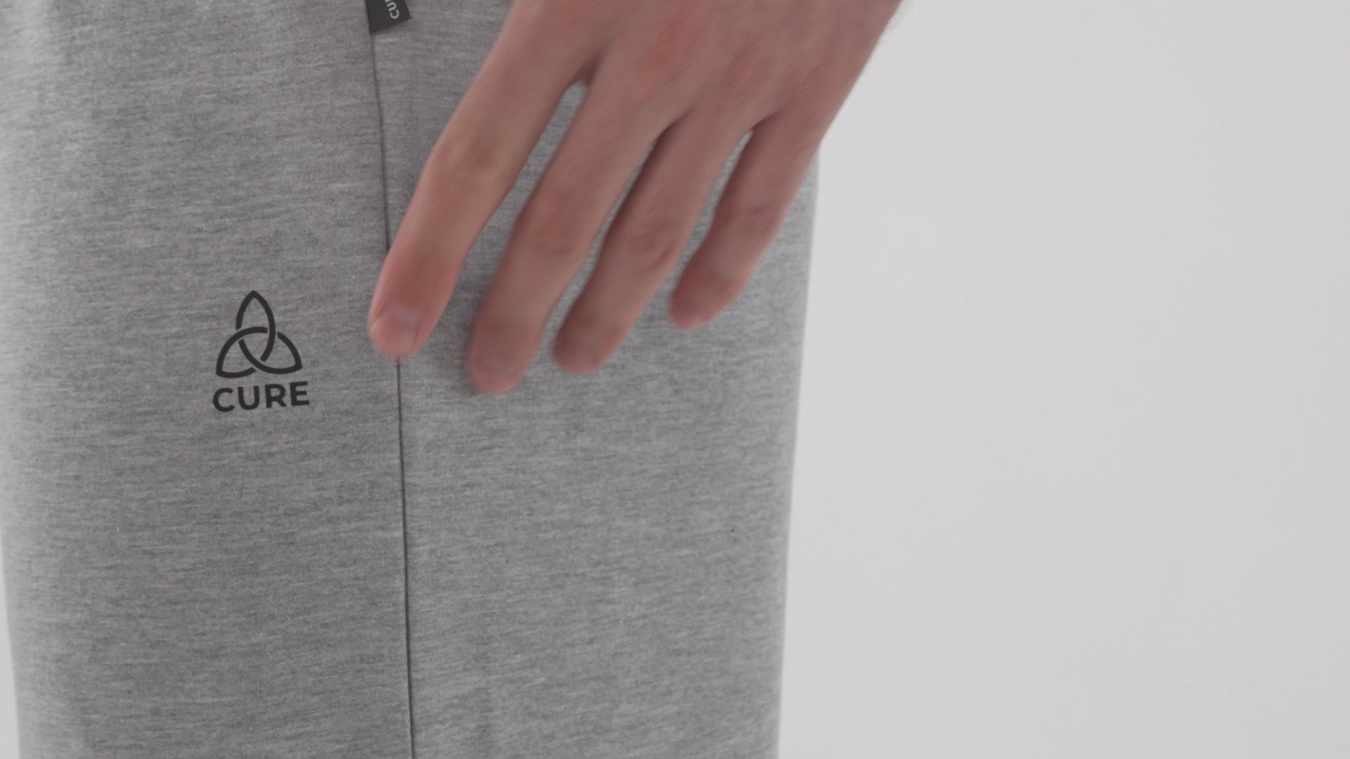 ComfortCure Video, Grau meliert, Detailansicht einer Pflegehose mit CURE-Logo, eine Hand berührt den Stoff