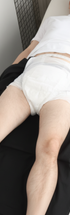 ComfortCure Adaptive Pflegehose für bettlägerige Patienten mit Klettverschluss, Schwarz, Aufsicht liegend, Hose heruntergezogen, Inkontinenzvorlage sichtbar